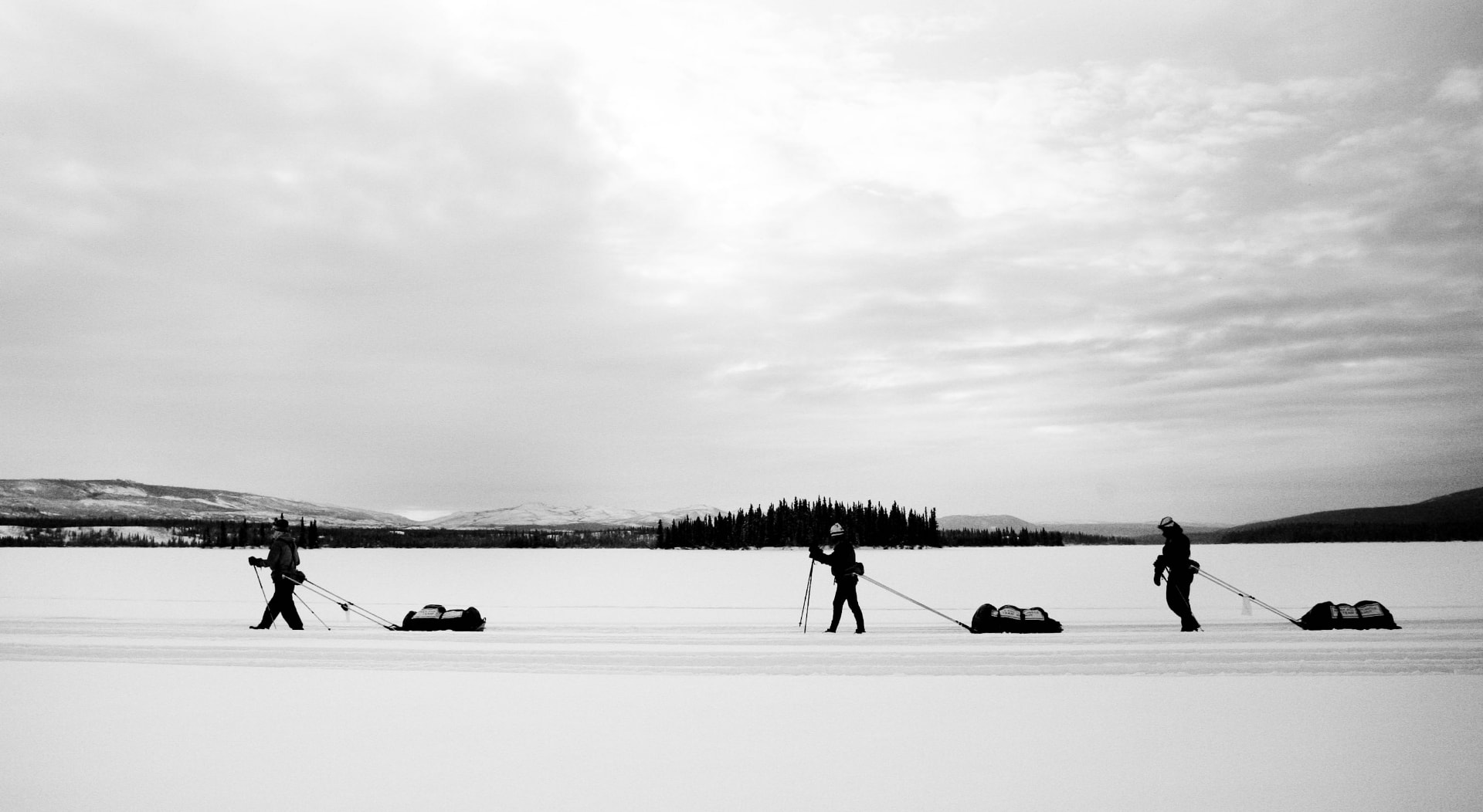 Three ultra athletes hauling sleds across a frozen lake in the Yukon Arctic Ultra